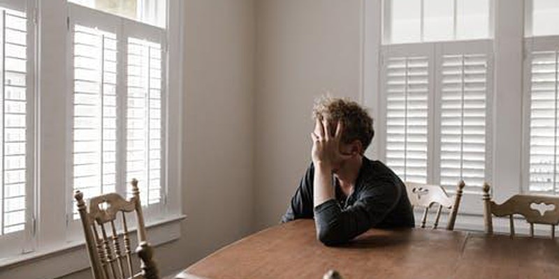 man sitting at table with hand on face